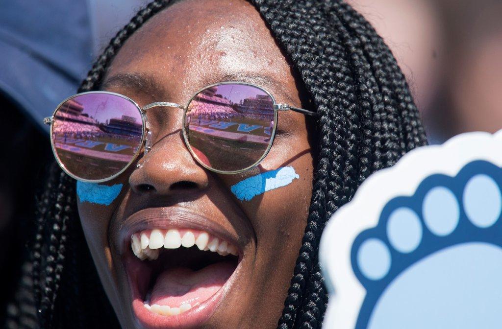 A black female student holding a Tar Heel-shaped foam finger cheers on the U.N.C. football team.